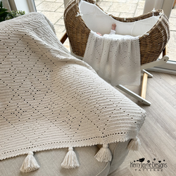 Crocheted blanket with tassels on a surface next to a wicker crib.