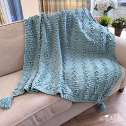 Blue knitted blanket with tassels on a beige couch in a living room setting.