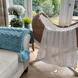 Crocheted blanket draped over a chair and sofa in a bright room with plants and flowers.