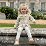 Young girl wearing a crocheted cardigan sitting on a stone bench in a garden.