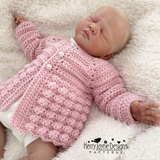 Newborn baby wearing a pink crocheted cardigan on a white fluffy surface, with 'Kerry Jayne Designs' branding.