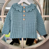 Blue crocheted jacket with buttons on a hanger in front of a mirror