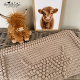 A chunky highland cow blanket folded on a wicker trunk