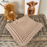 a highland cow crochet blanket folded on a wicker trunk 