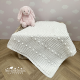 White crocheted blanket with pink plush toy on a wooden surface against a heart-patterned wall.