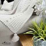 White textured blanket with tassels on a sofa next to a potted plant