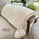 White crochet blanket with tassels on a sofa, featuring Kerry Jayne Designs branding.