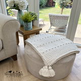 Cushioned ottoman with a textured blanket draped over it, in a room with a view of a garden.
