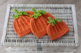 3 orange pumpkin shaped crochet hats displayed on a wicker trunk 