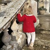 Child in a red crochet sweater standing on stone steps outdoors