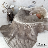Baby wrapped in a textured blanket with a plush toy in the background