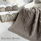 Crocheted blanket with a decorative border next to yarn balls in a basket.
