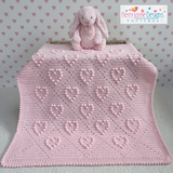 Pink knitted blanket with heart pattern and a pink bunny toy on a light blue background with heart patterns.