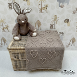 Stuffed animal on a woven box with a knitted blanket, against a wallpapered wall with animal prints.