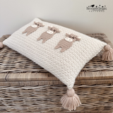 Close-up of a crochet cushion featuring three brown cow appliqués with cream faces and horns on a cream knit background. 