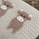 Close-up of a crocheted blanket featuring two brown cow appliqués with cream faces and horns on a cream knit background. 